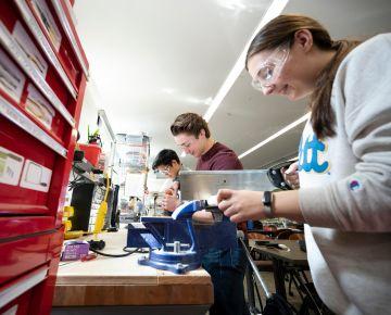 Three Pitt engineering students stand at a workbench and use tools