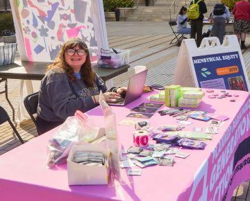 A student sits at an informational table about menstrual equity