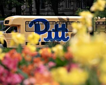 A Pitt shuttle travels through Oakland with blooming flowers in the foreground.