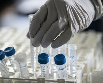 A gloved hand handles vials of liquid.
